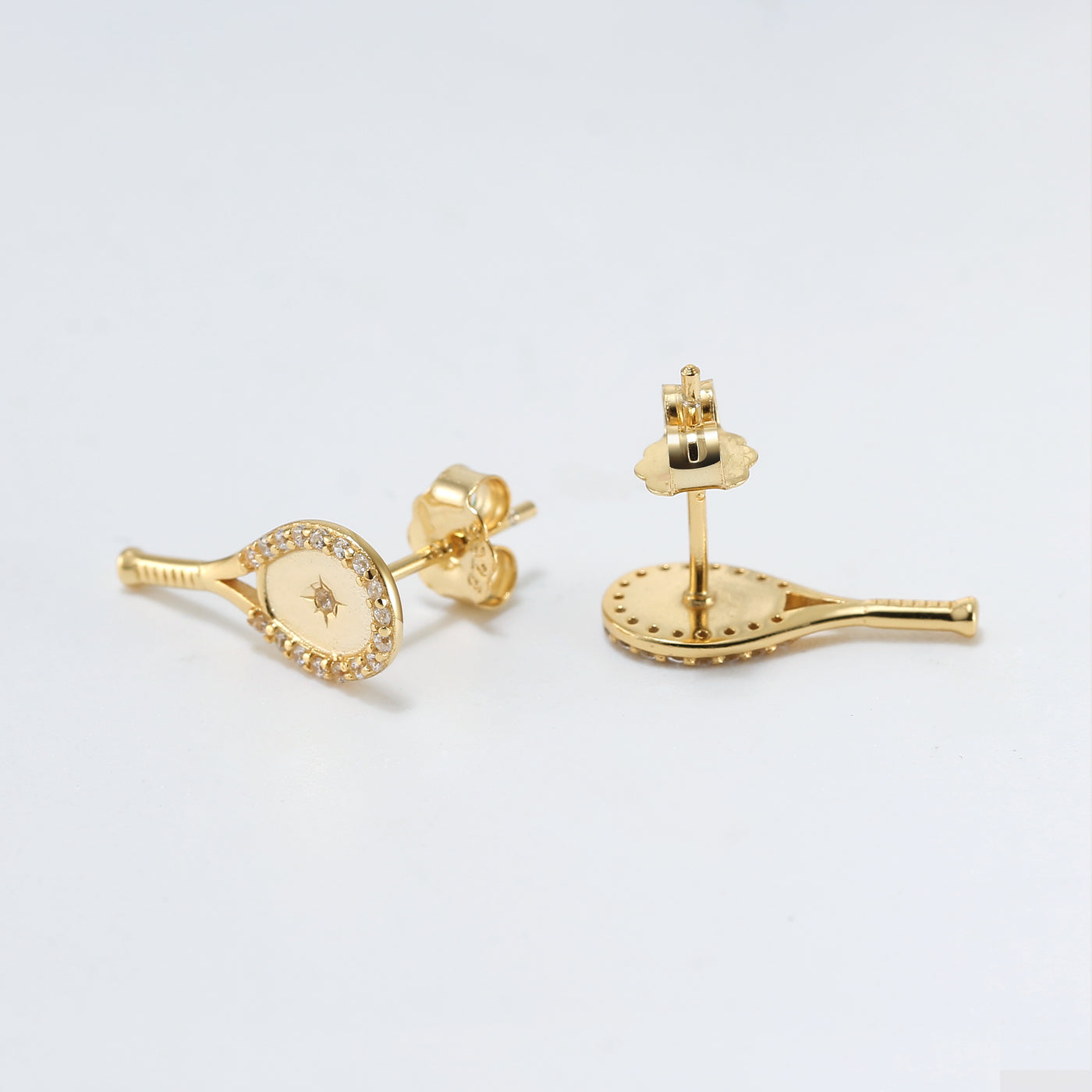 Tennis Racquet Plus Stud Earrings in Gold by LoveMatch. These tennis earrings feature A classic racquet shape with a set crystal and impact starburst design in the center, and framed with delicate top-quality CZ crystals. 15mm long.