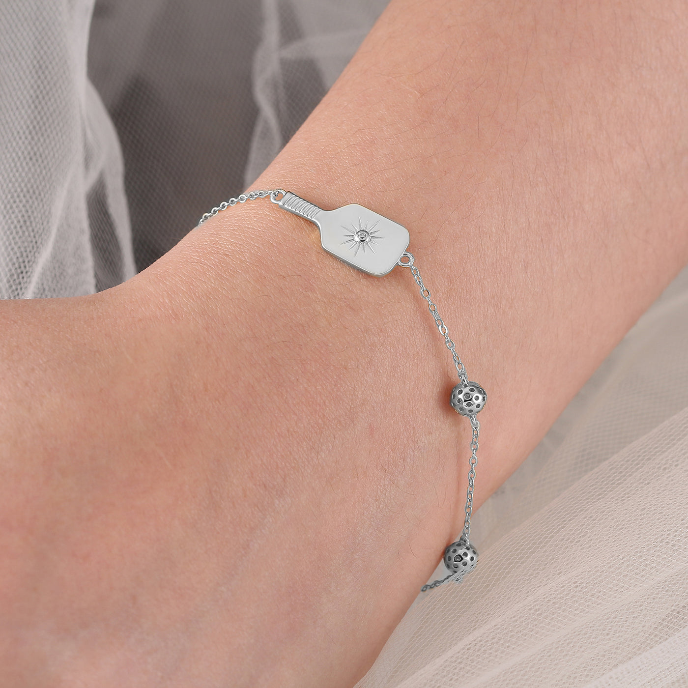 Silver Pickleball Play It Forward Bracelet featuring our "Dainty Dinker" charm front and center with three tiny pickleballs around it. Made from sustainably sourced sterling silver with a protective rhodium plating.
