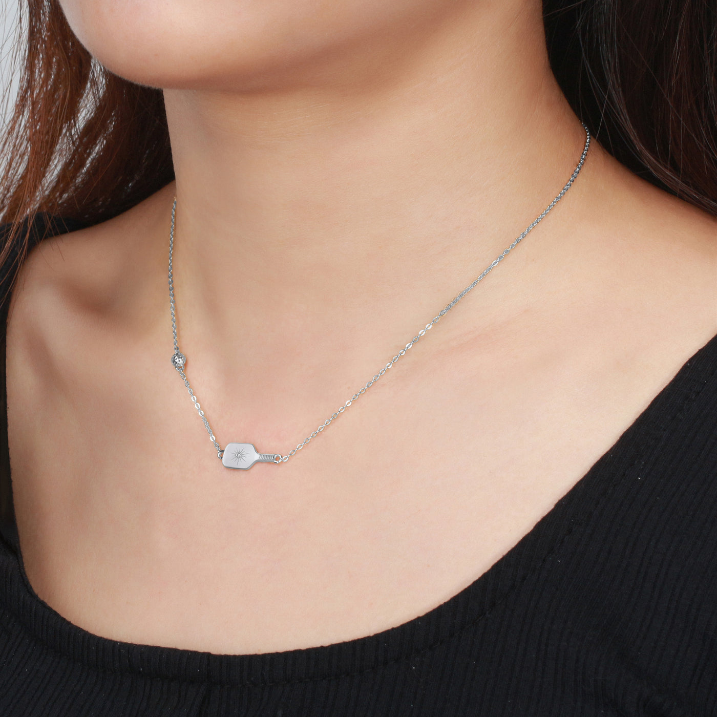 Pickleball Paddle and Ball dainty Necklace in Sterling Silver. A more delicate version of the Dinker, The Dainty Dinker is a 3D detailed, sporty and chic necklace that is perfect on its own or as a layered piece as part of your jewelry wardrobe. Made from sustainably sourced sterling silver with a protective rhodium plate.  Top quality CZ stones are set in the center of the paddle, and the pickleball charm is set into the chain .