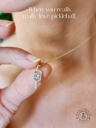 Gold necklace with a pickleball paddle pendant held by a hand, with text 'When you really, really love pickleball' above.