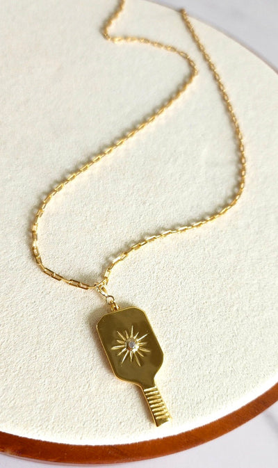 Gold Pickleball Grande Paddle Pendant Charm. This elegant charm features a realistic pickleball paddle in a 18k gold overlaid on a solid sterling silver charm with a crystal-centered starburst design. Spring clip allows you to attach this to your favorite necklace or bracelet, or anywhere you can think of!