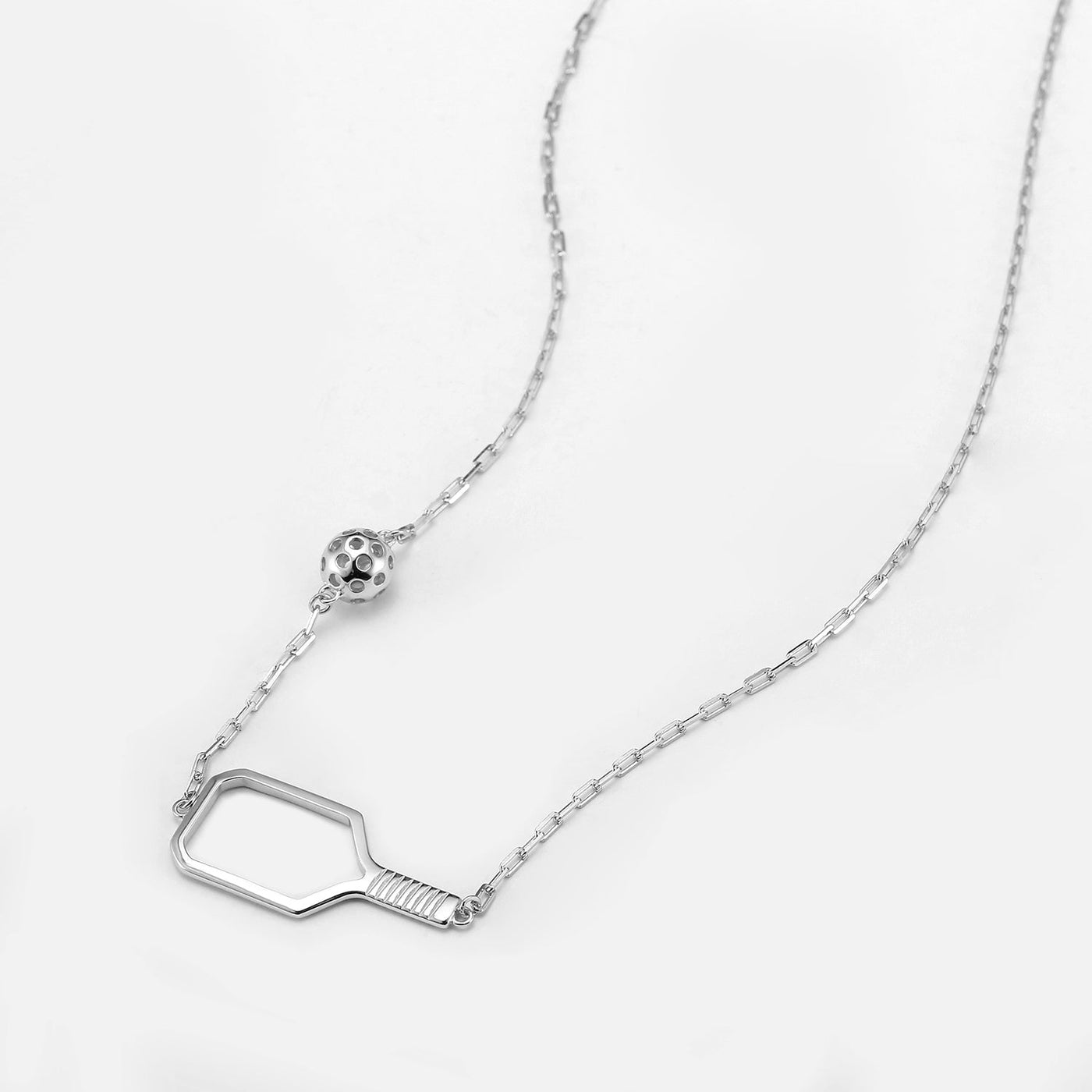 Pickleball Playset Silver Necklace. A faceted gold open concept paddle sits like an elegant pendant with the detailed pickleball resting up the chain. Made from sustainably sourced Sterling Silver with a protective rhodium overlay&nbsp; - comes on a modern paper clip chain.