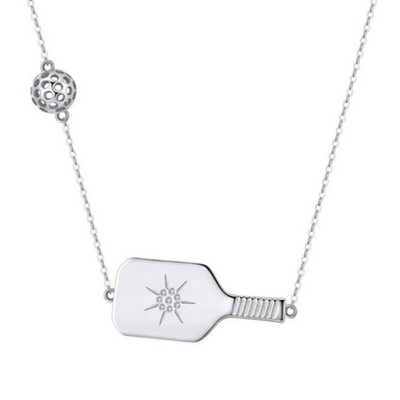 Pickleball The Cross Court Silver Necklace. The Cross Court necklace is a unique design as the paddle sits nicely on the décolletage and the pickleball sits slightly further up near the wearer's pulse point. We set in a top-quality CZ stone with a starburst design at the paddle center, the paddle can easily be flipped over for a more subtle design as well. Made from sustainably sourced Sterling Silver, paired with a delicate but sturdy clip chain that adds a touch of contemporary style.